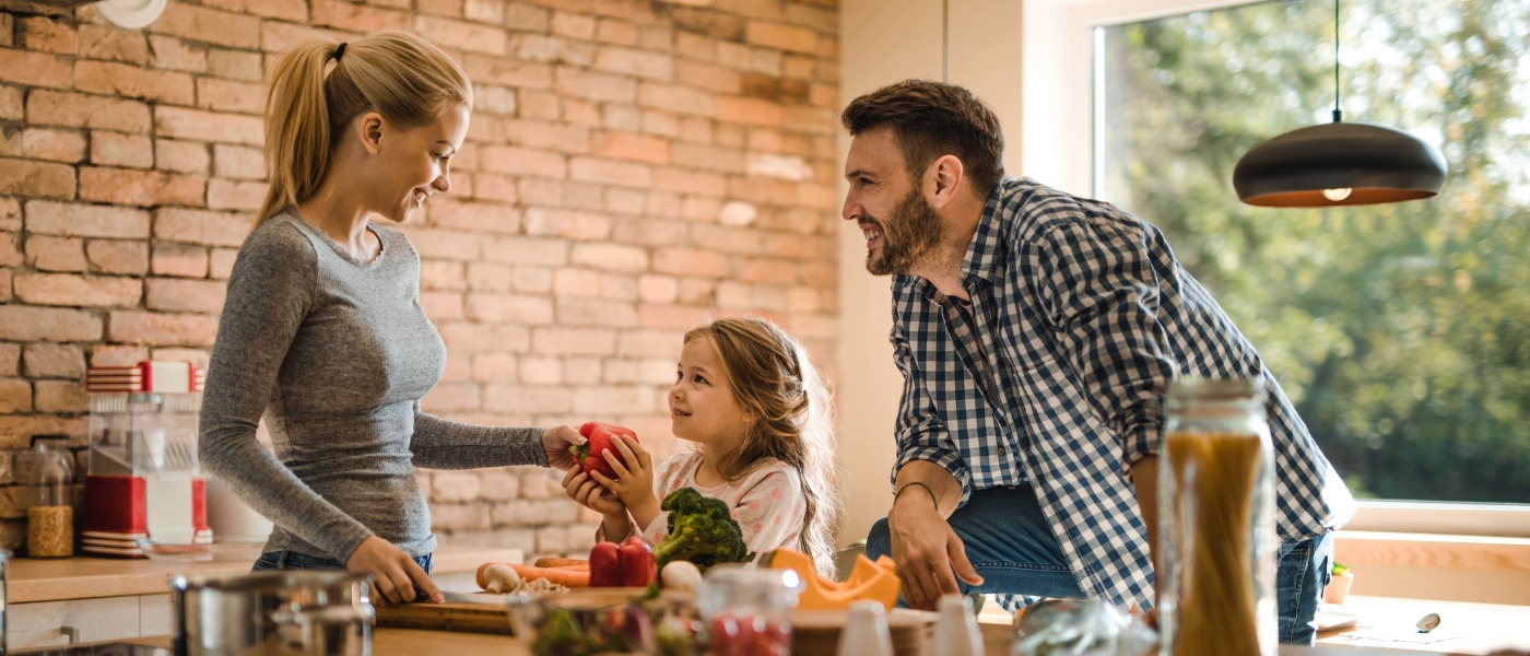 Happy parents preparing healthy snack with their daughter in the kitchen.