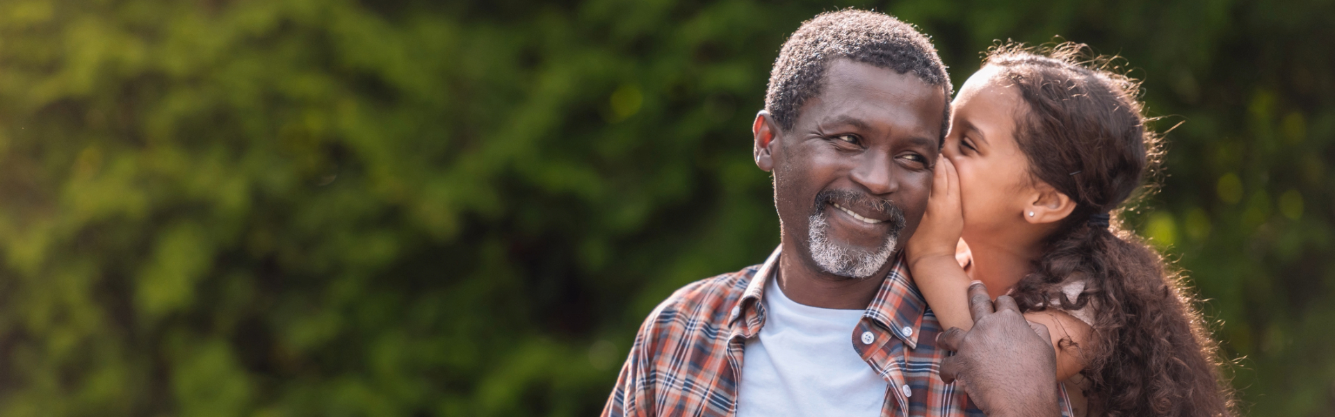 Girl whispering to her grandfather while sitting on bench in park