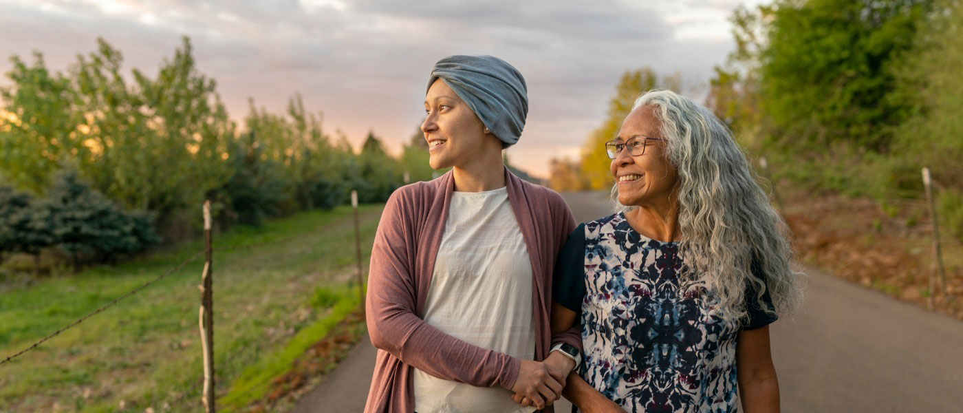 Woman with cancer strolling arm-in-arm with another woman during a sunset